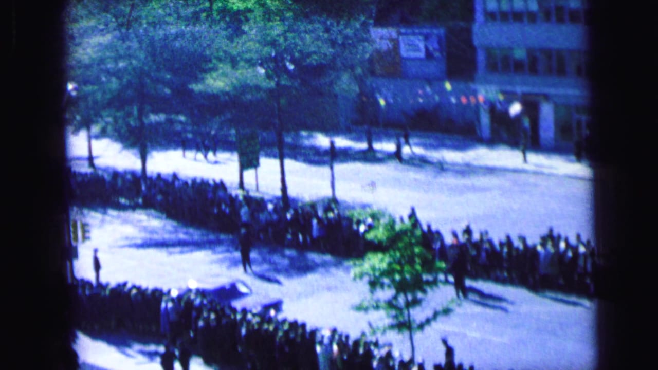 1964 Camden street scene with a dense sidewalk crowd, trees, building fronts, and strong sunlight.