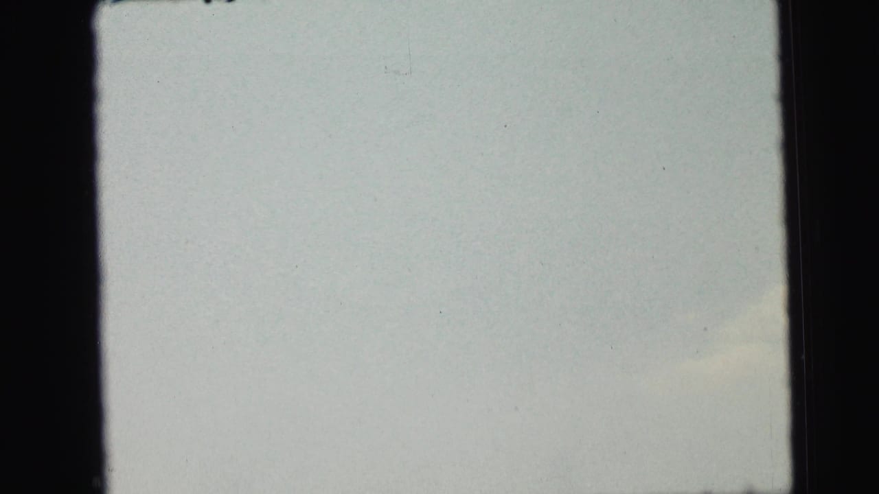 1964 Camden 8mm frame showing mostly pale sky with faint cloud coloration, dark vertical borders, and scattered film dust or scan marks.