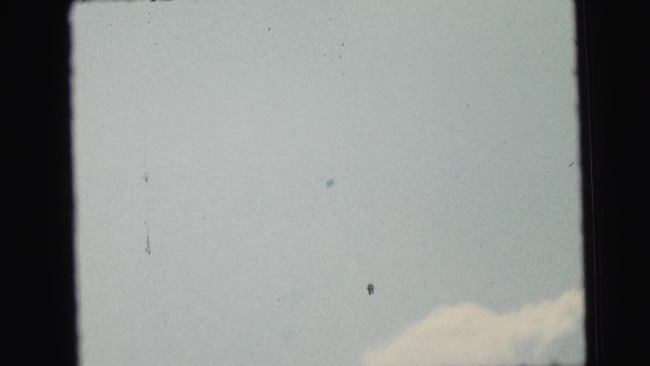 1964 8mm home-movie frame from Camden metadata showing pale sky, faint cloud, dust specks, and dark film borders.