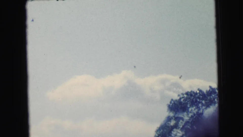 1964 Camden 8mm frame showing soft clouds, pale sky, a dark tree edge, and visible film-frame borders.