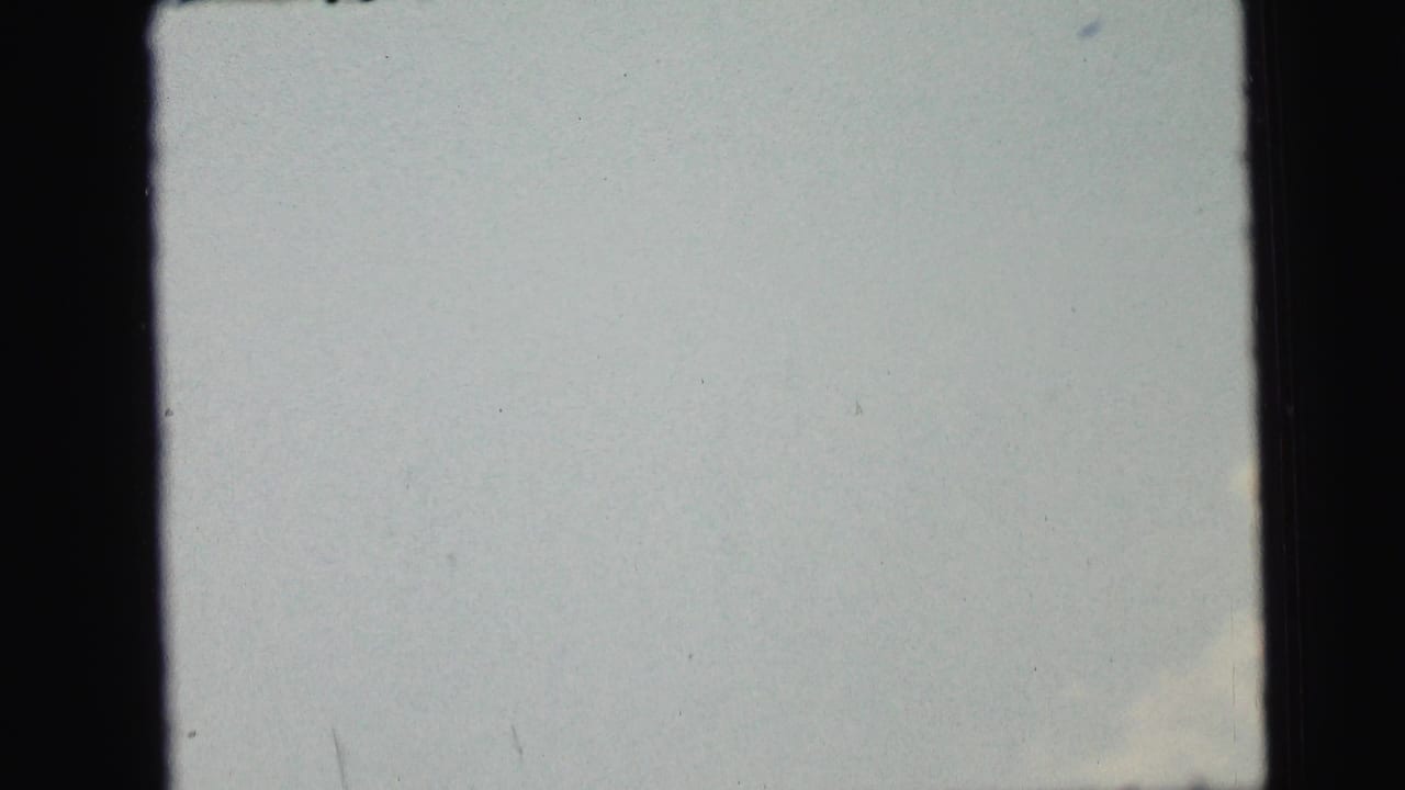 1964 8mm home-movie frame from Camden metadata with a washed pale sky, faint lower cloud, and dark gate edges.