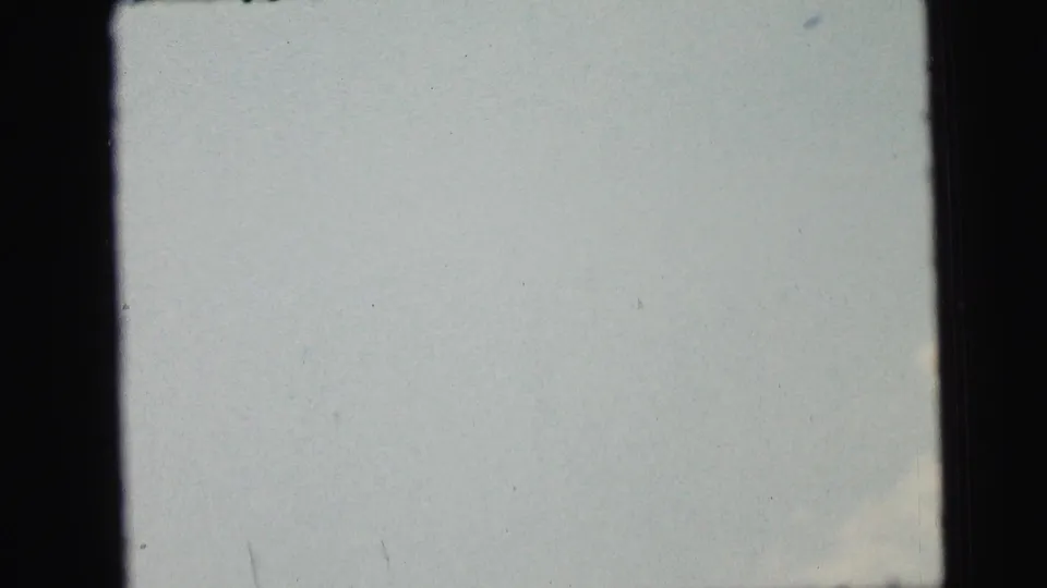 1964 8mm home-movie frame from Camden metadata with a washed pale sky, faint lower cloud, and dark gate edges.