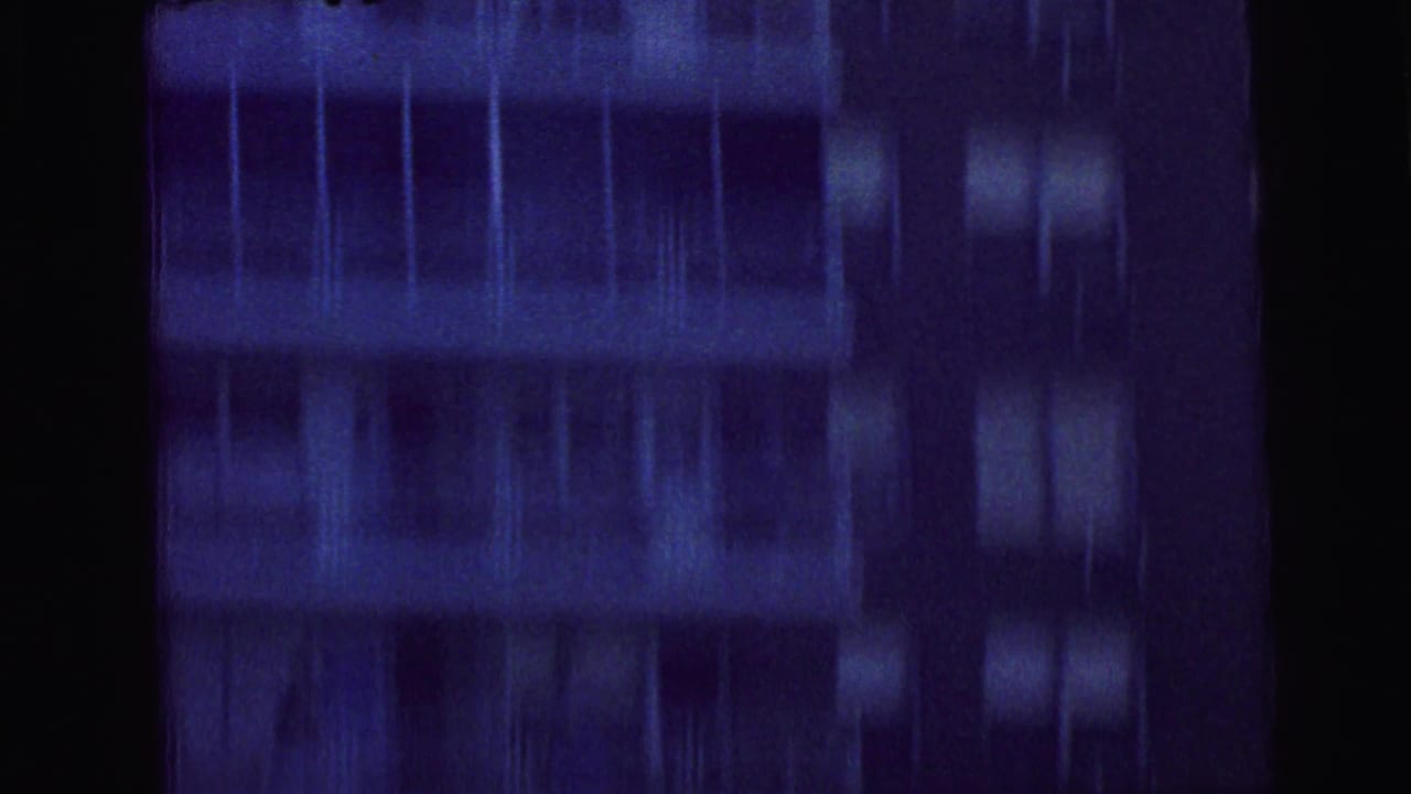 1964 Camden 8mm frame with blurred helicopter movement above or beside a dark apartment building facade with rows of windows.