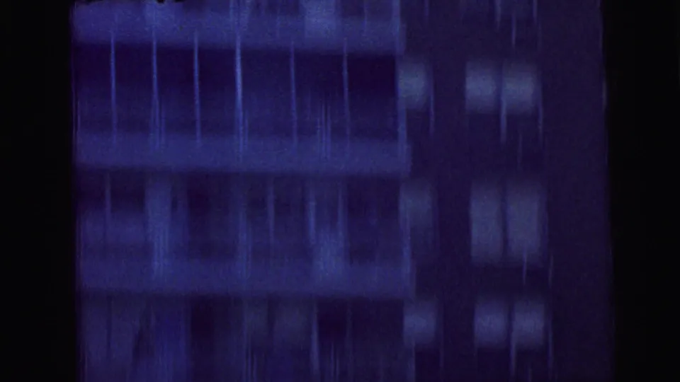 1964 Camden 8mm frame with blurred helicopter movement above or beside a dark apartment building facade with rows of windows.