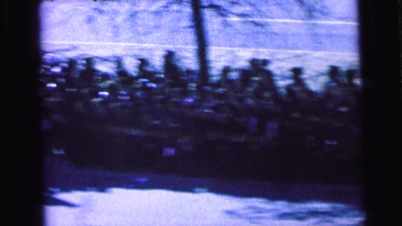 Blurred crowd lining a bright street behind dark window or screen bars.