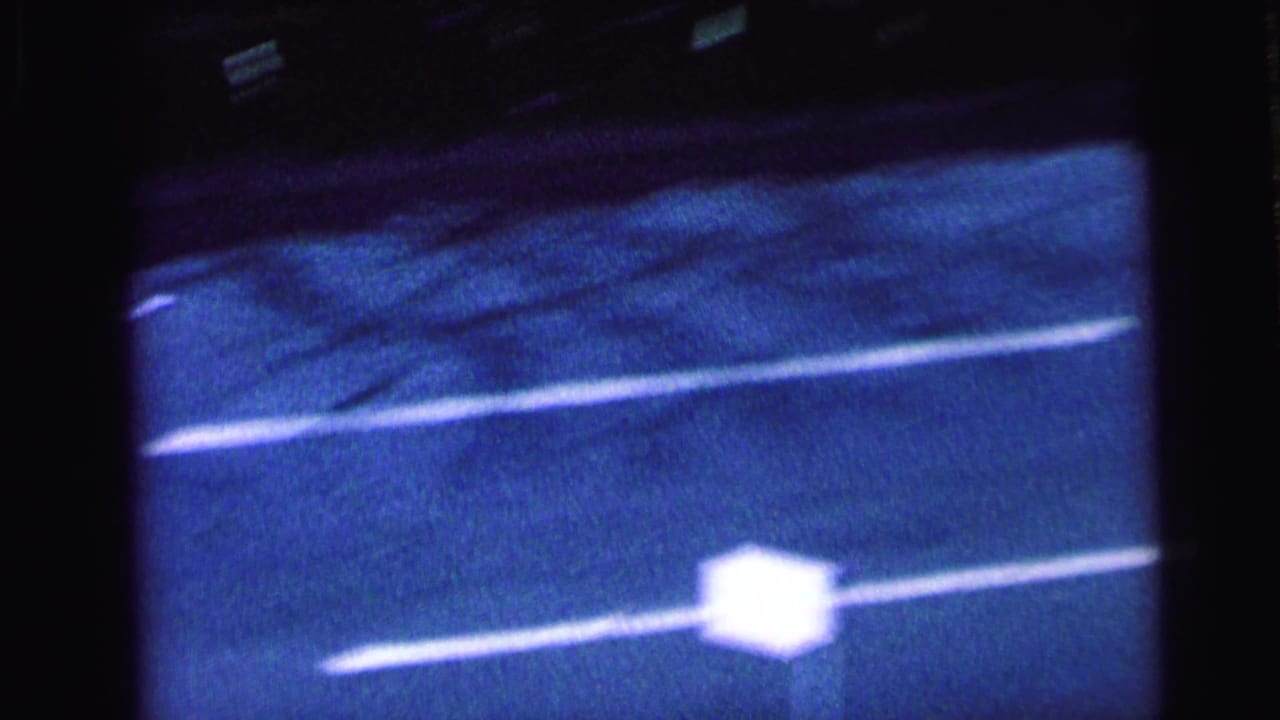Blue-tinted 8mm view of the street and lane markings as the motorcade camera movement loses the vehicles briefly.