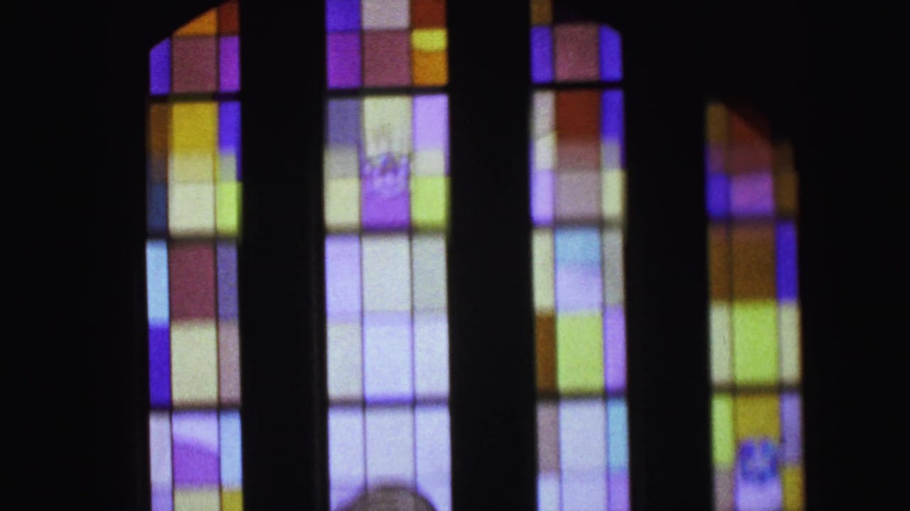 Tall stained glass windows glow in a dark church interior.