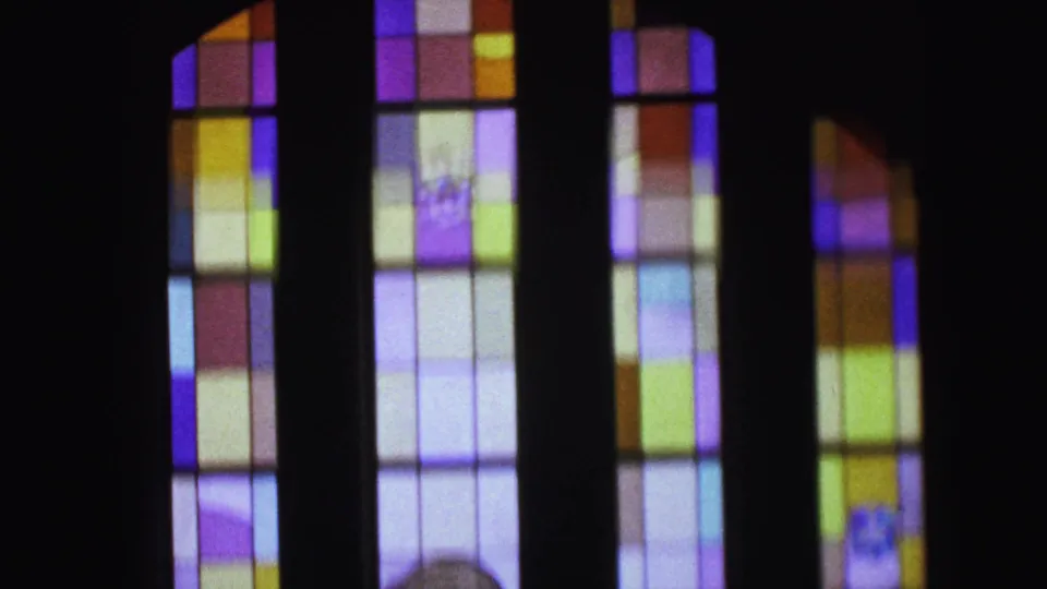 1964 Camden home-movie frame showing colorful stained glass windows in a dim church interior.