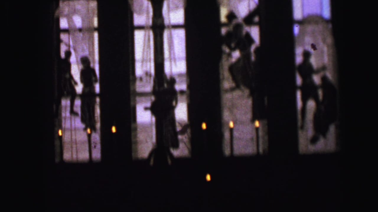 Silhouetted people stand near candlelit church windows.