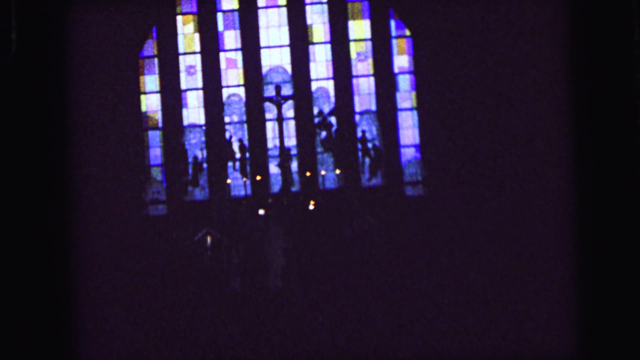 1964 Camden 8mm frame with distant stained glass, shadowed figures, and candlelight in a church interior.