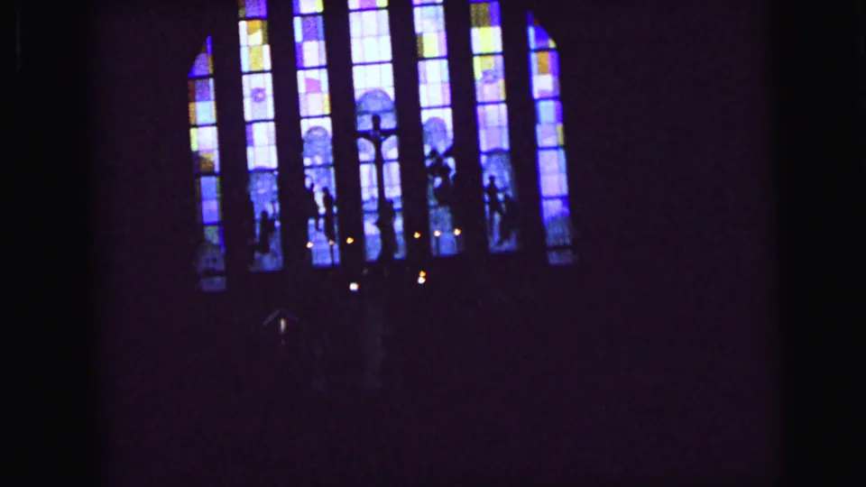 1964 Camden 8mm frame with distant stained glass, shadowed figures, and candlelight in a church interior.