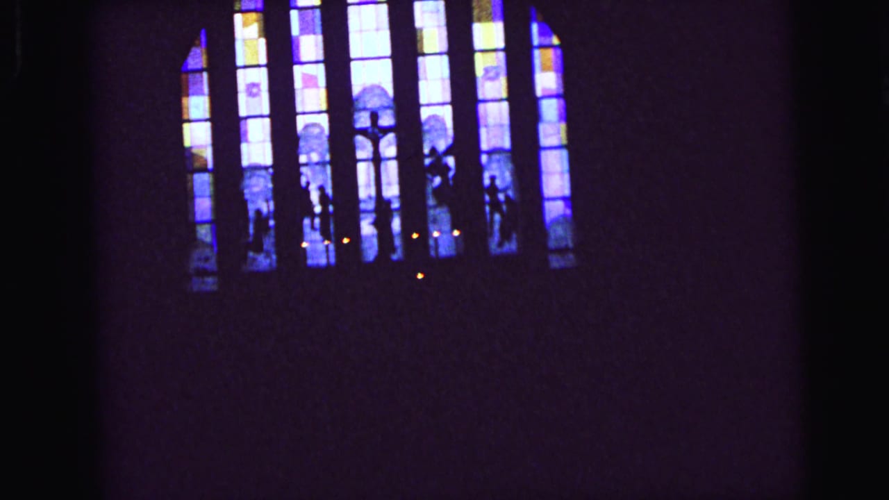 Final 1964 Camden church frame showing blue-purple stained glass, silhouettes, and small candles in deep shadow.