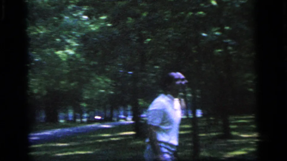 A man in a light blue shirt appears in the wooded Camden park, partly blurred by handheld 8mm motion and low light.