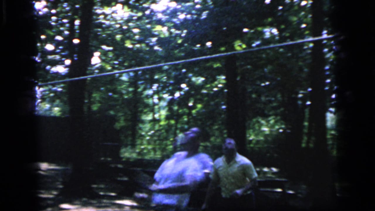 Three adults appear in a shaded Camden, New Jersey wooded clearing in 1964, with one holding a racket during casual badminton play.