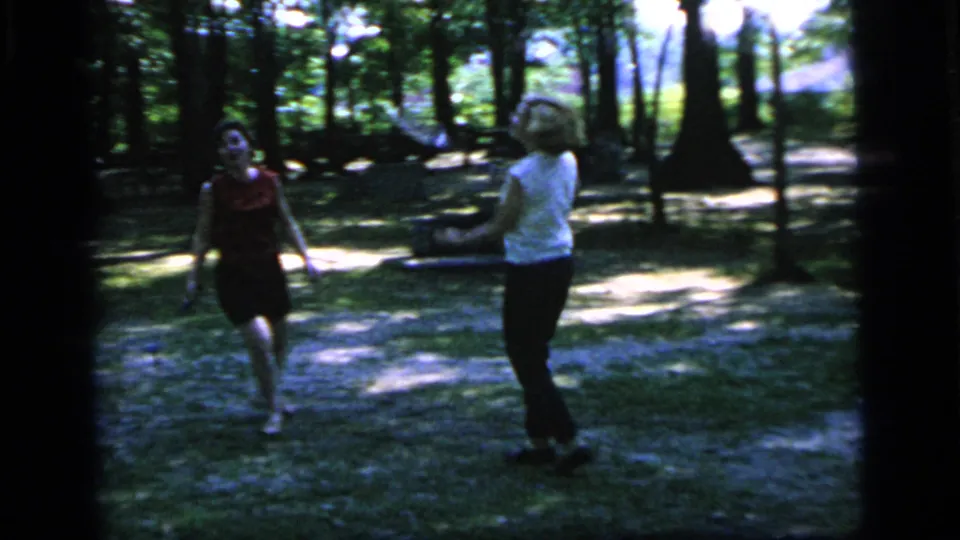 The badminton game continues in 1964 Camden, New Jersey footage, with two women standing amid trees and patchy sunlight.
