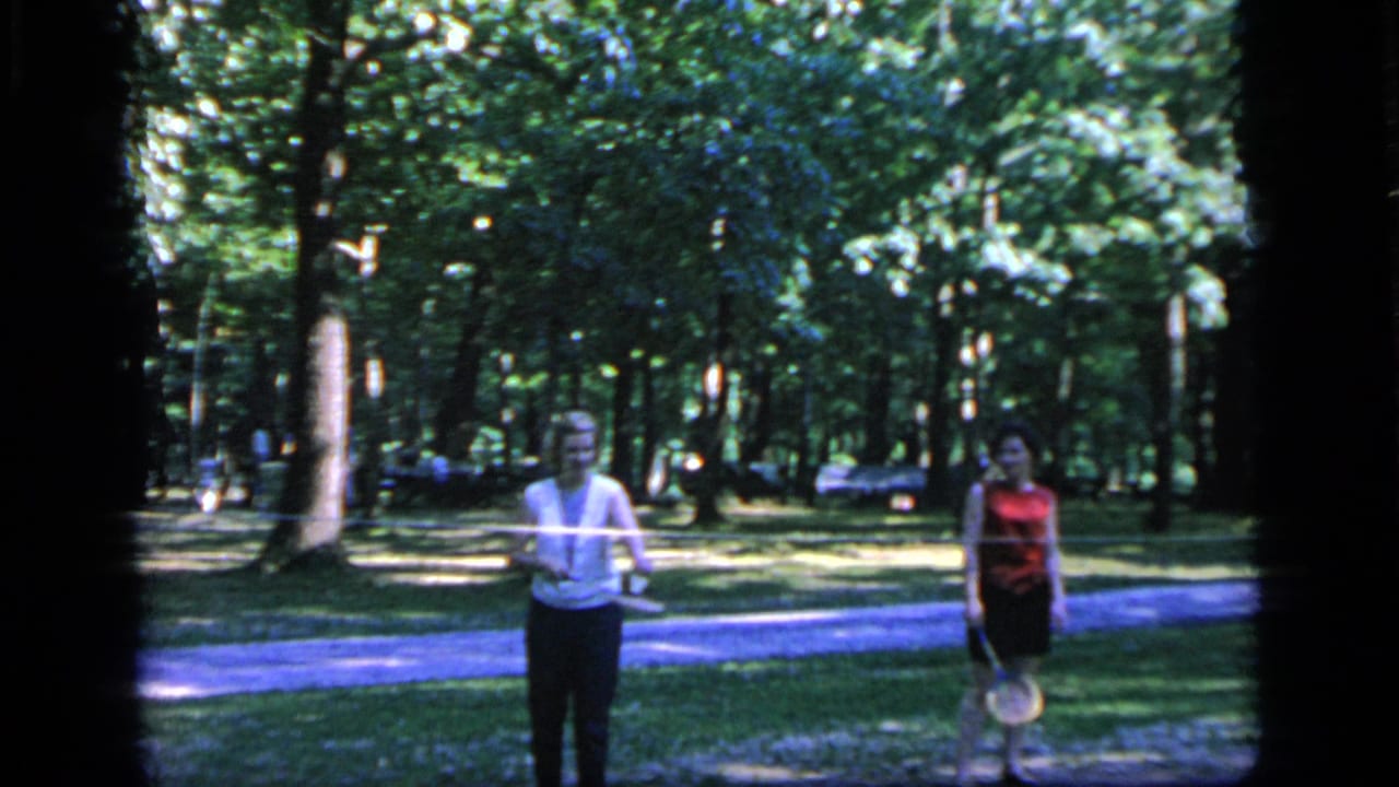 In Camden, New Jersey in 1964, two women with badminton rackets stand on a grassy area beneath tall trees.