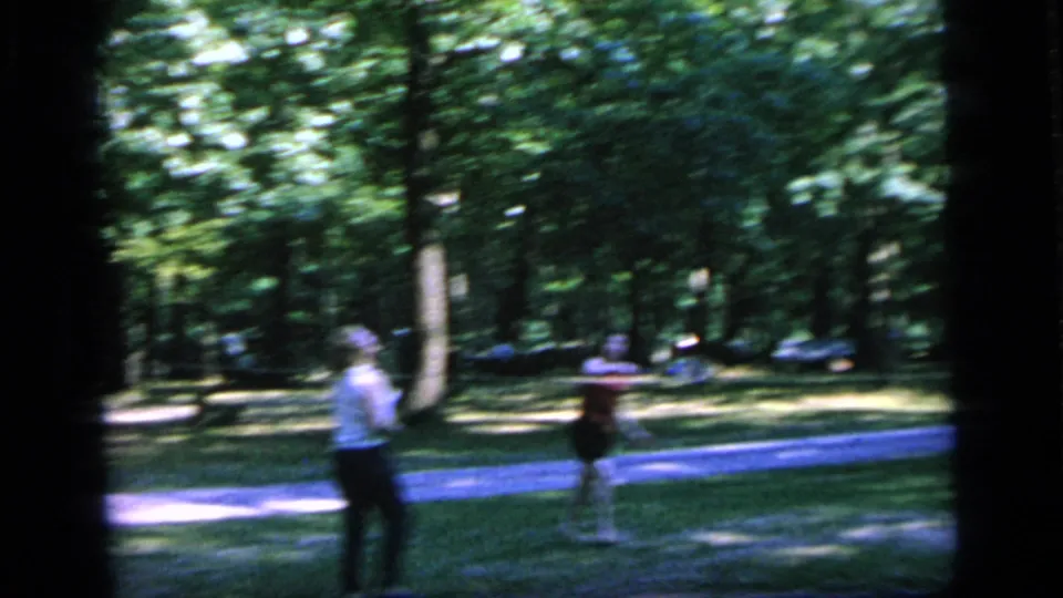 1964 Camden home-movie frame with three women positioned around a badminton game beside a blue path and trees.