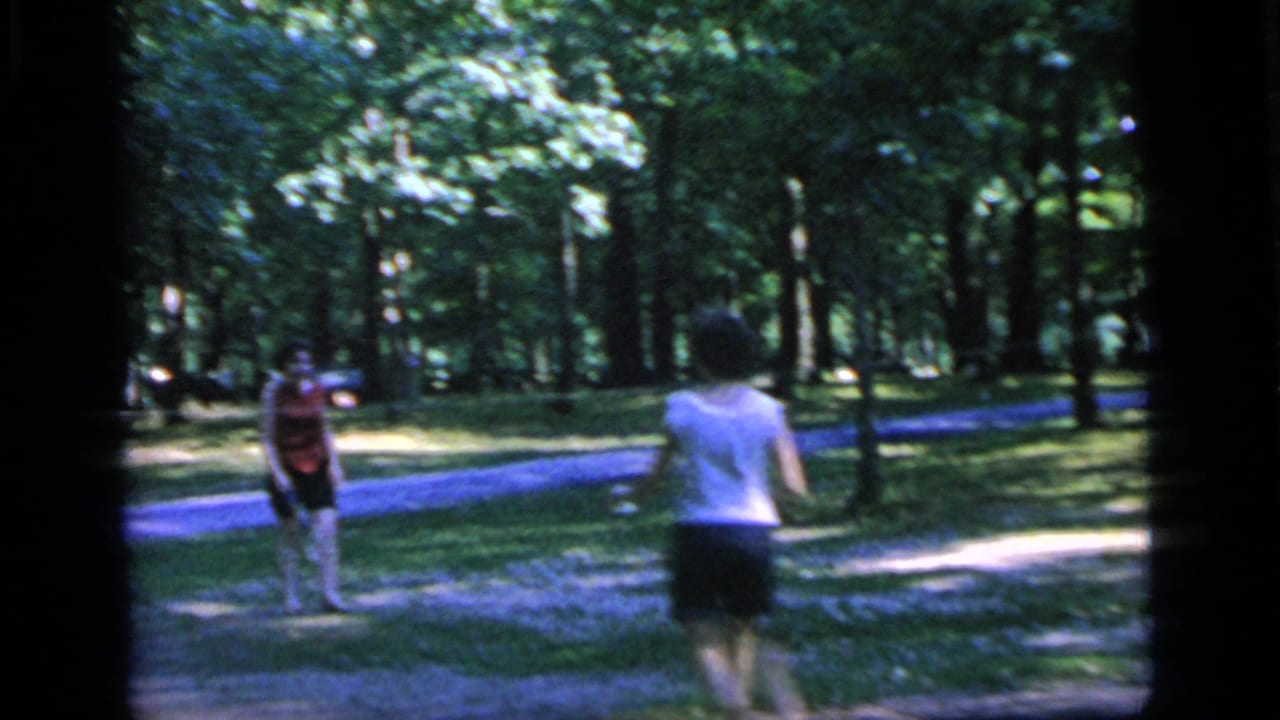 Two adults face each other with rackets near a winding park path and trees.
