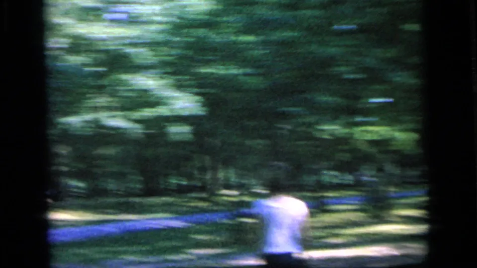 A fast handheld pan blurs a white-shirted tennis player against trees and grass in the 1964 park footage.