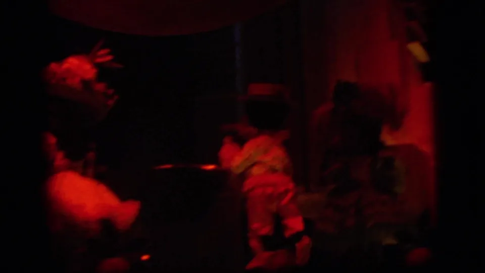 Low-light 8mm frame from the Camden clip showing silhouetted visitors in a red-lit performance or display area.