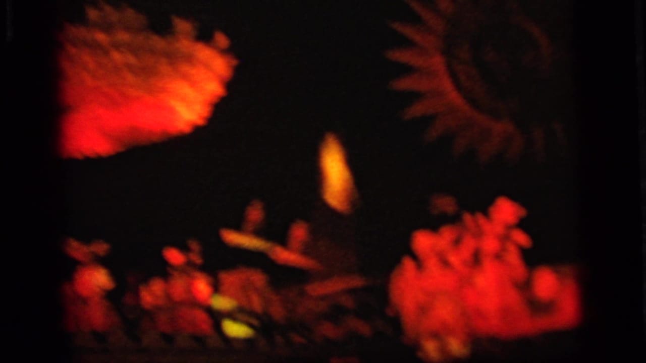 Low-light 8mm view of red illuminated scenery and small toy-like figures in the Camden amusement display.