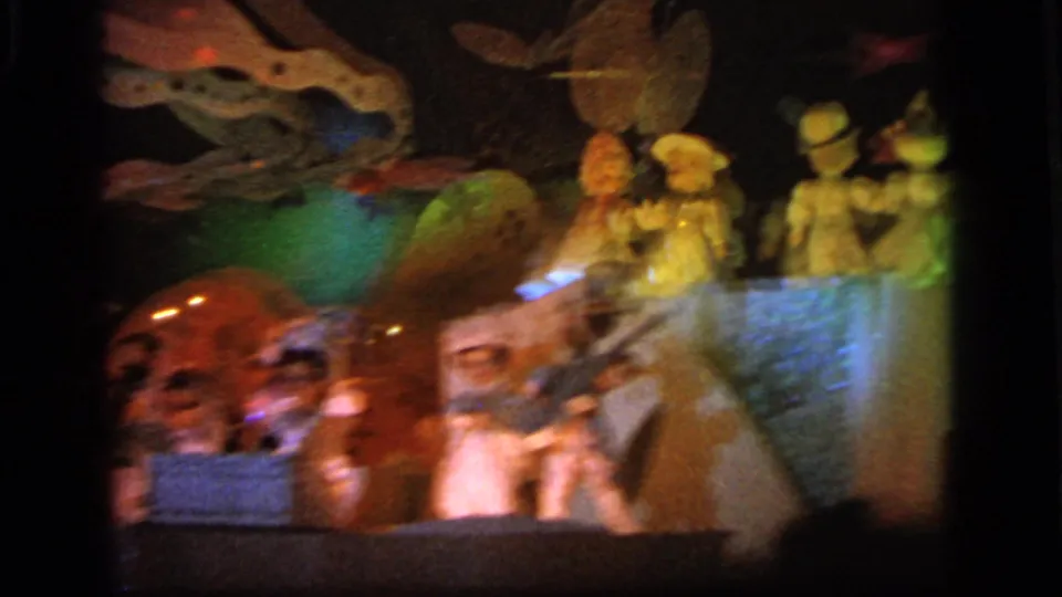 1964 home-movie frame showing painted miniature figures, skull-like forms, and green-blue light inside an amusement attraction display.