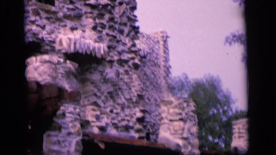 Home-movie close view of a Camden stone building, showing rough masonry, an arched opening, roof trim, and surrounding trees.