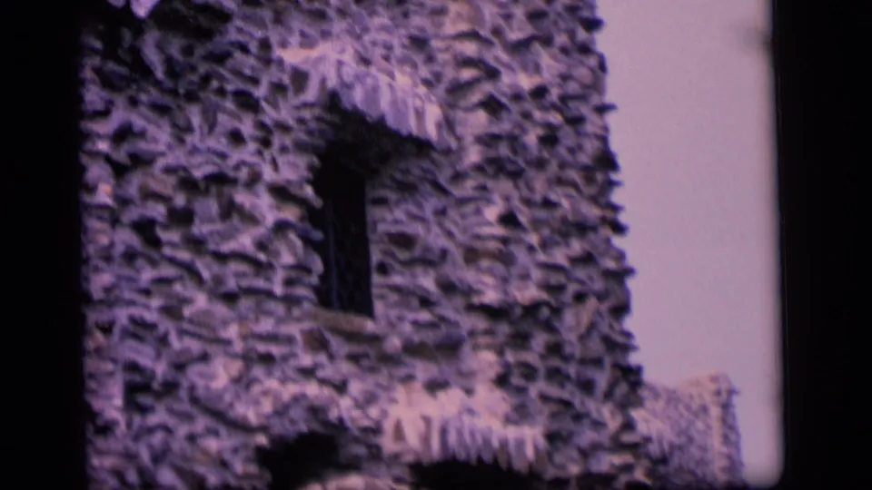 1964 Camden home-movie frame of a stone facade with a small window, arched lower opening, roof edge, and soft color shift.