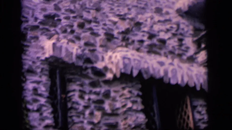 1964 Camden home-movie frame showing lower stonework, narrow windows, and a band of scalloped thatch-like trim.