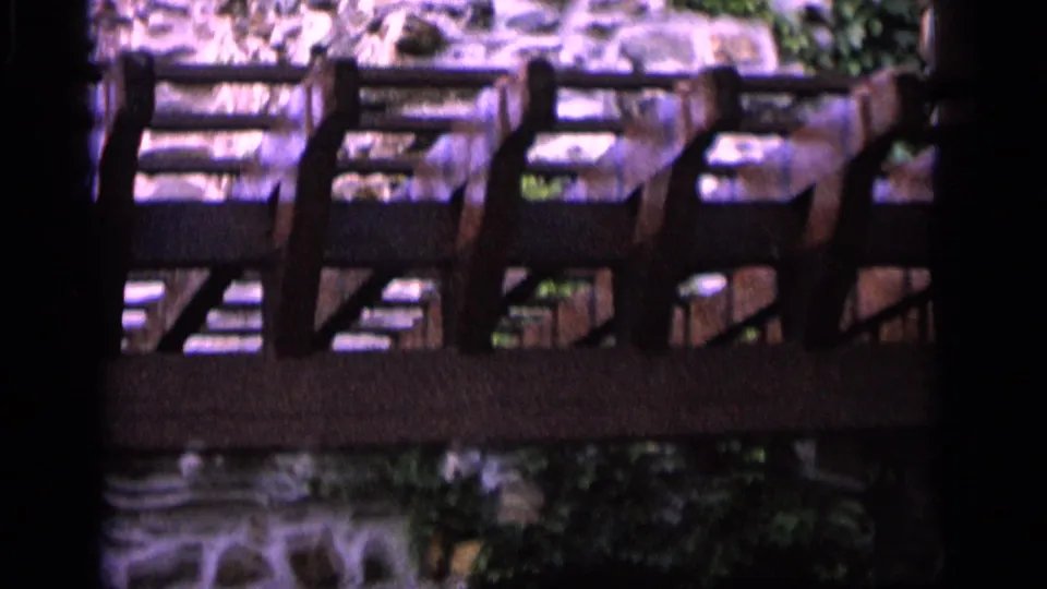 1964 Camden frame with a dark wooden railing across rough stonework and greenery, scanned from 8mm film.