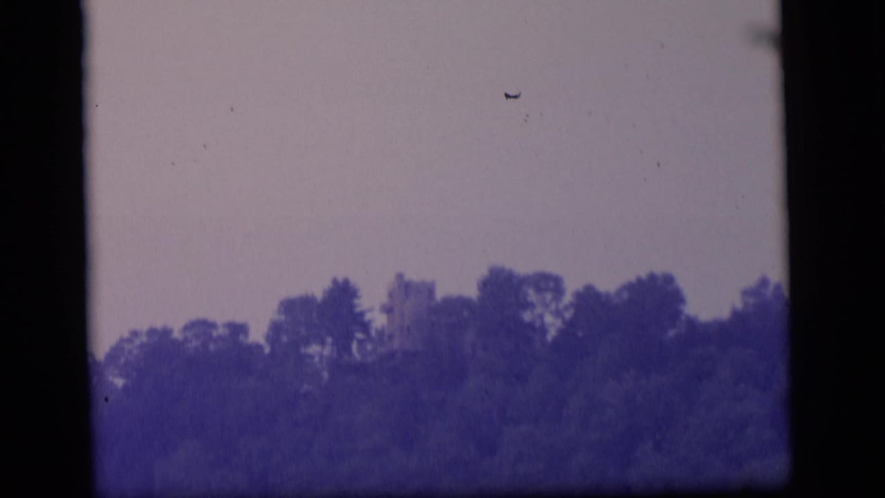 1964 Camden, New Jersey 8mm frame showing a dark treeline, pale sky, faint structure, and visible film borders.
