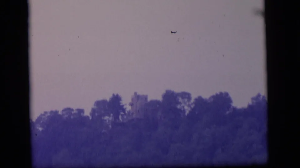 1964 Camden, New Jersey 8mm frame showing a dark treeline, pale sky, faint structure, and visible film borders.