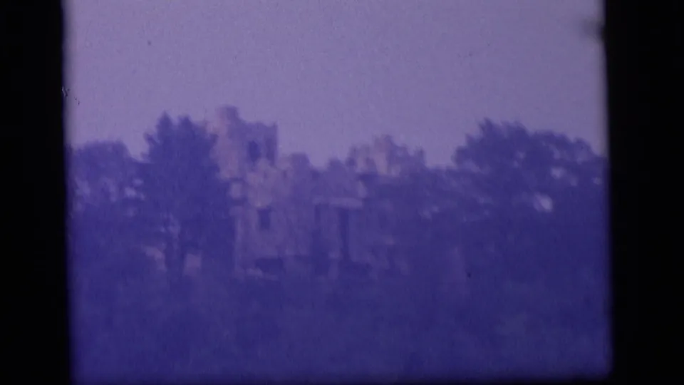 1964 Camden home-movie frame with a ruined building partially obscured by foliage and heavy purple 8mm color shift.