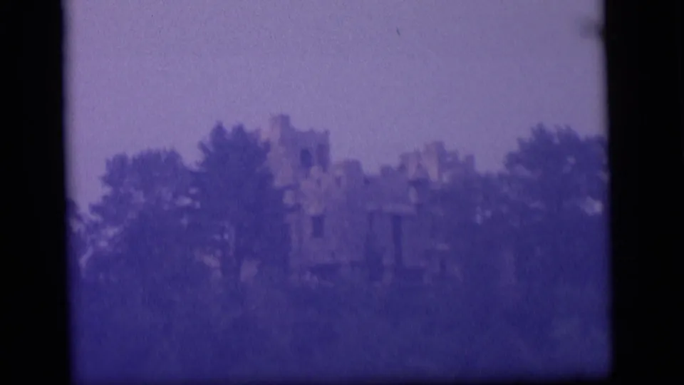 Distant 1964 Camden 8mm view of a ruin behind trees, framed by dark film edges and a subdued sky.