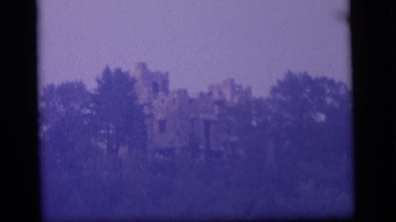 1964 8mm Camden, New Jersey lake view with trees partly obscuring a distant castle-like structure.