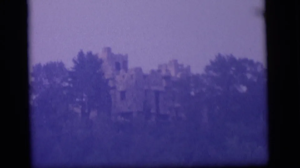 1964 8mm Camden, New Jersey lake view with trees partly obscuring a distant castle-like structure.