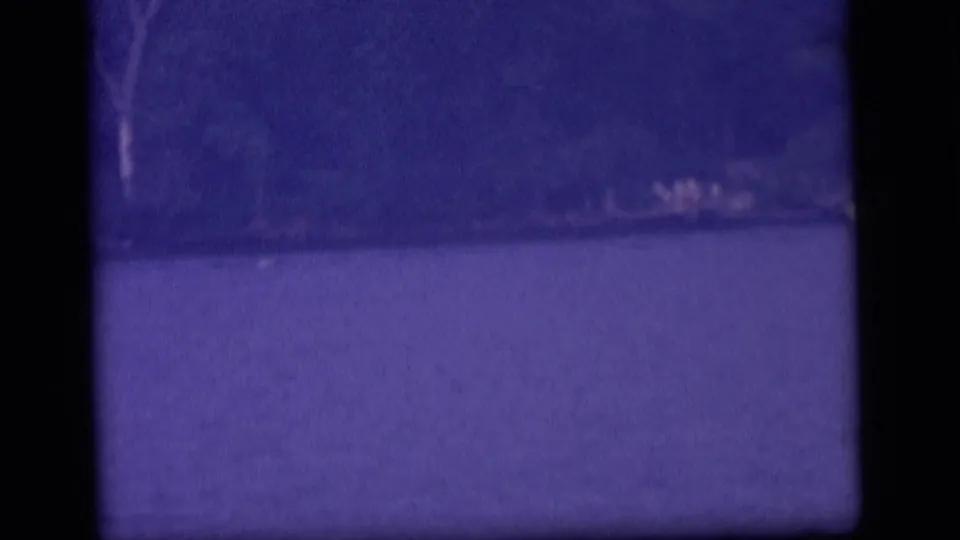 Purple-tinted 1964 8mm view of lake water and a wooded shoreline in Camden, New Jersey.