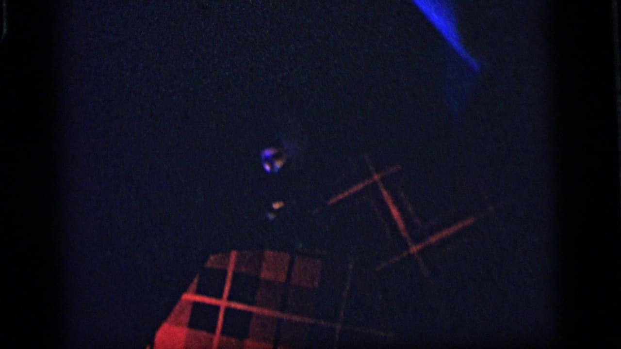 1964 Camden 8mm frame showing red plaid fabric or shade forms against a dark blue, underexposed interior.