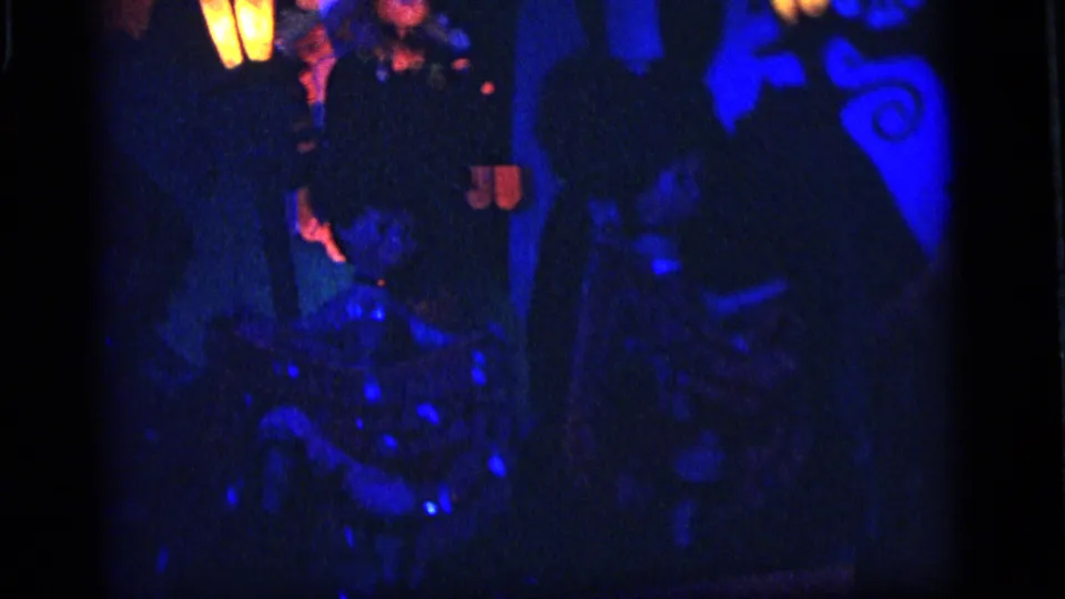 Low-light 1964 Camden frame showing puppet forms in blue shadow with red highlights and small glowing yellow stage shapes.