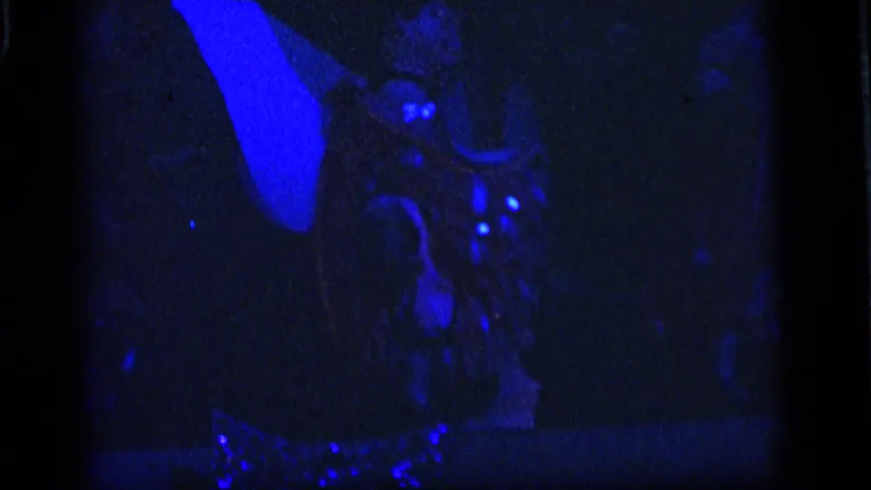 Underexposed 1964 Camden ride frame with blue-lit silhouettes, faint decorative shapes, and reflective points in a dark attraction space.