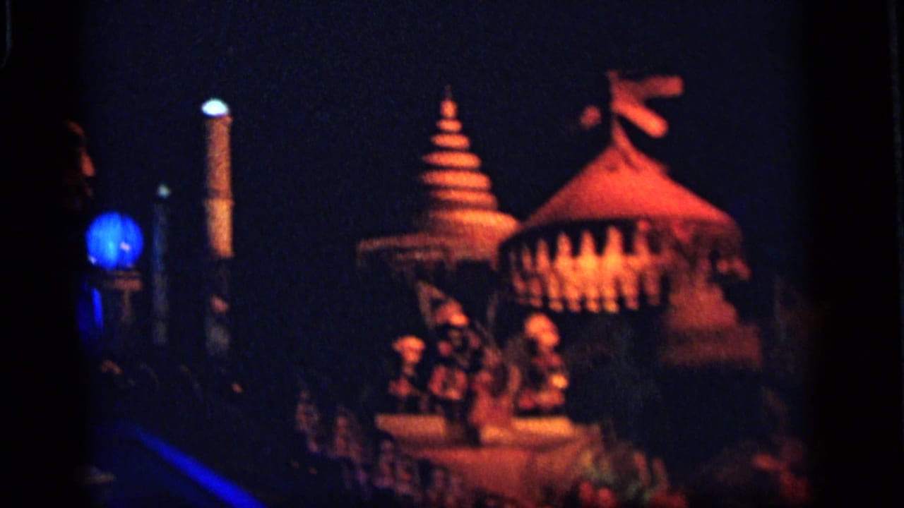 1964 Camden home-movie frame showing red-lit tiered and domed structures with small figures in a dark nighttime festival setting.
