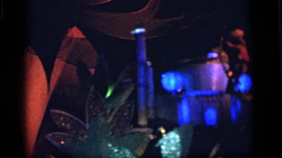 1964 Camden home-movie frame showing blue globe lights, a vertical column, and soft decorative forms in a dim festival scene.