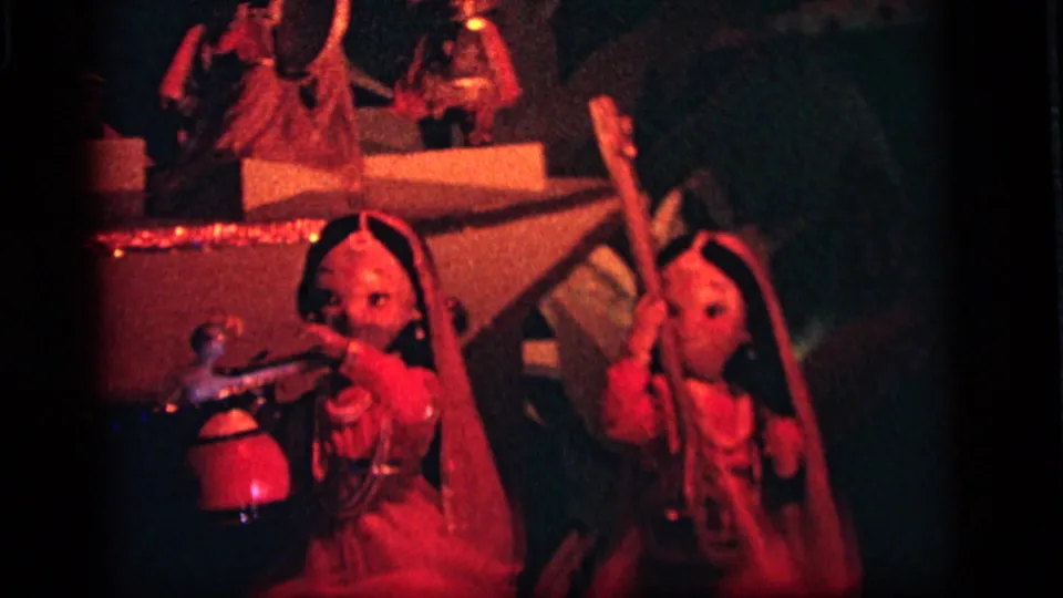 1964 Camden nighttime frame showing red-lit traditional-looking performer figures with raised arms, props, and a stage-like backdrop.