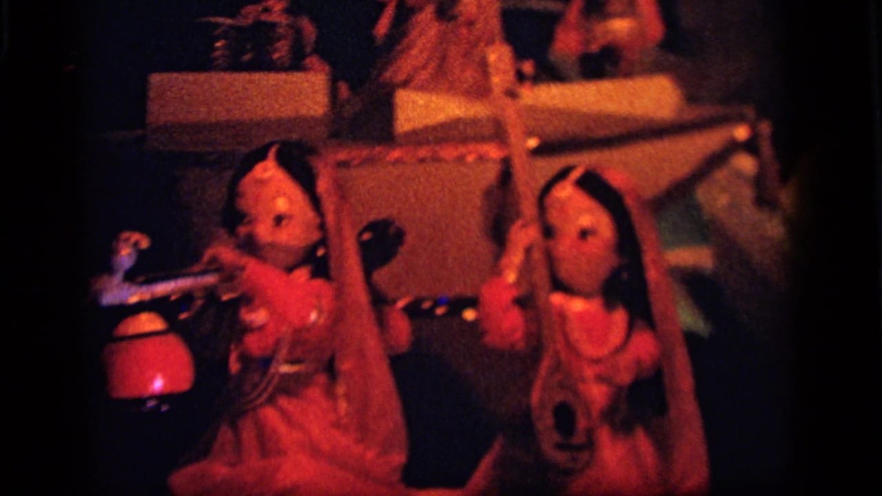 Camden 1964 home-movie frame showing costumed toy dolls in a dramatic red-lit miniature stage setting.