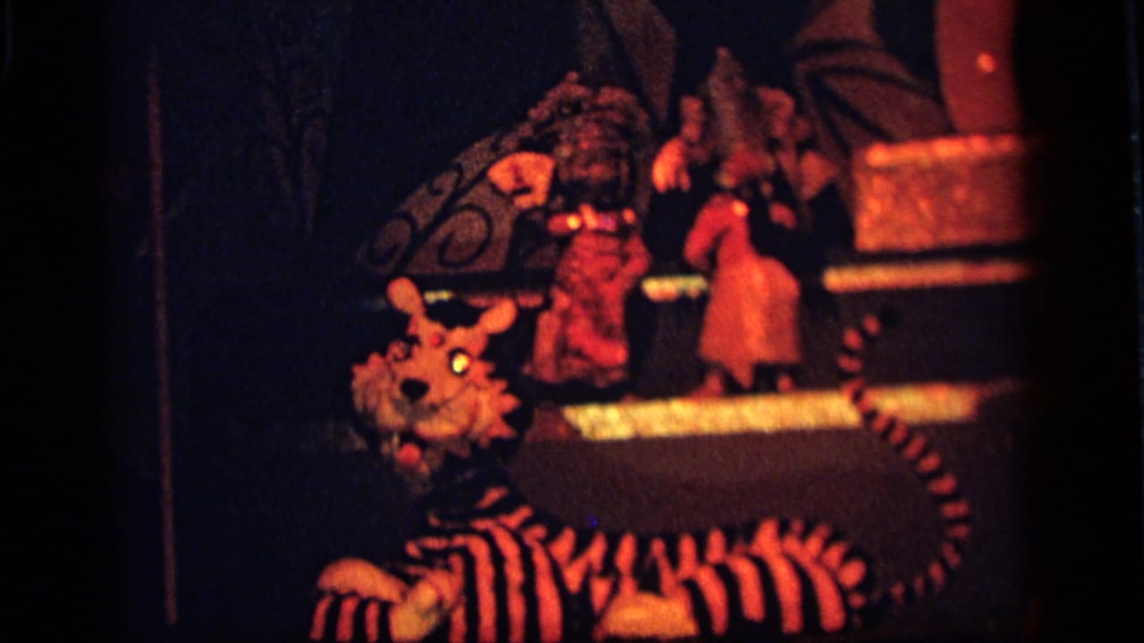 1964 Camden 8mm frame showing a striped tiger puppet in the foreground with costumed toy figures on a platform behind it.