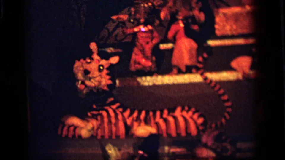 1964 Camden home-movie frame showing a large striped tiger figure on a dimly lit amusement display stage.