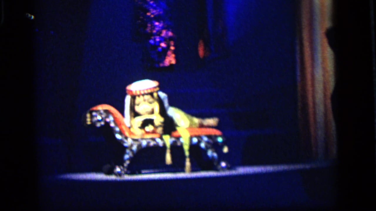 Costumed character figure rides a decorative mechanical horse in a blue-lit 1964 Camden amusement display.