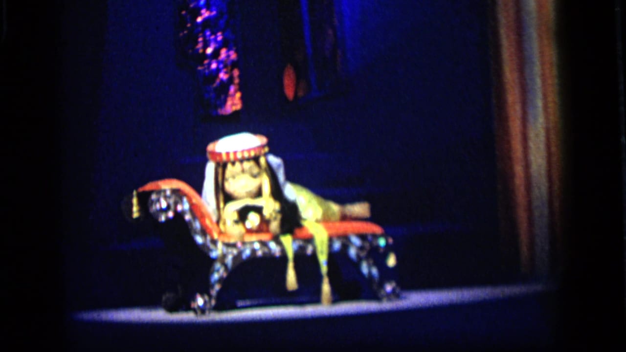 1964 Camden 8mm frame of a costumed rider figure on a decorated mechanical horse against a dark stage backdrop.