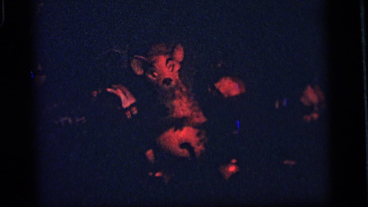1964 Camden frame showing a red-lit animatronic animal figure performing in a dark display, with surrounding shadowed forms.