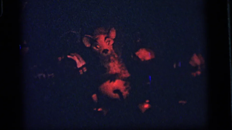 1964 Camden frame showing a red-lit animatronic animal figure performing in a dark display, with surrounding shadowed forms.